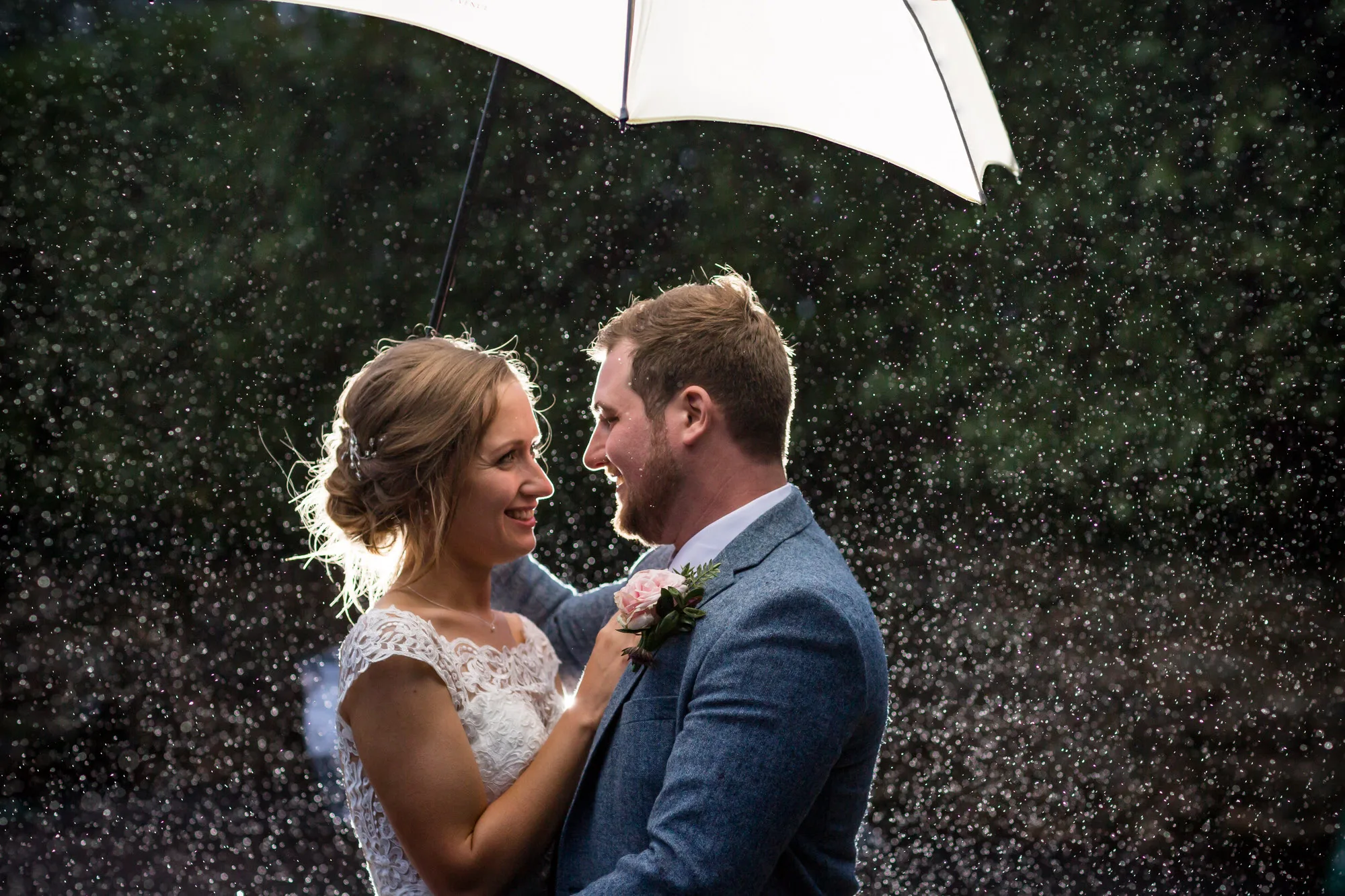 Sussex wedding photographer - a couple stand under a white umbrella in the rain at their wedding in West Sussex