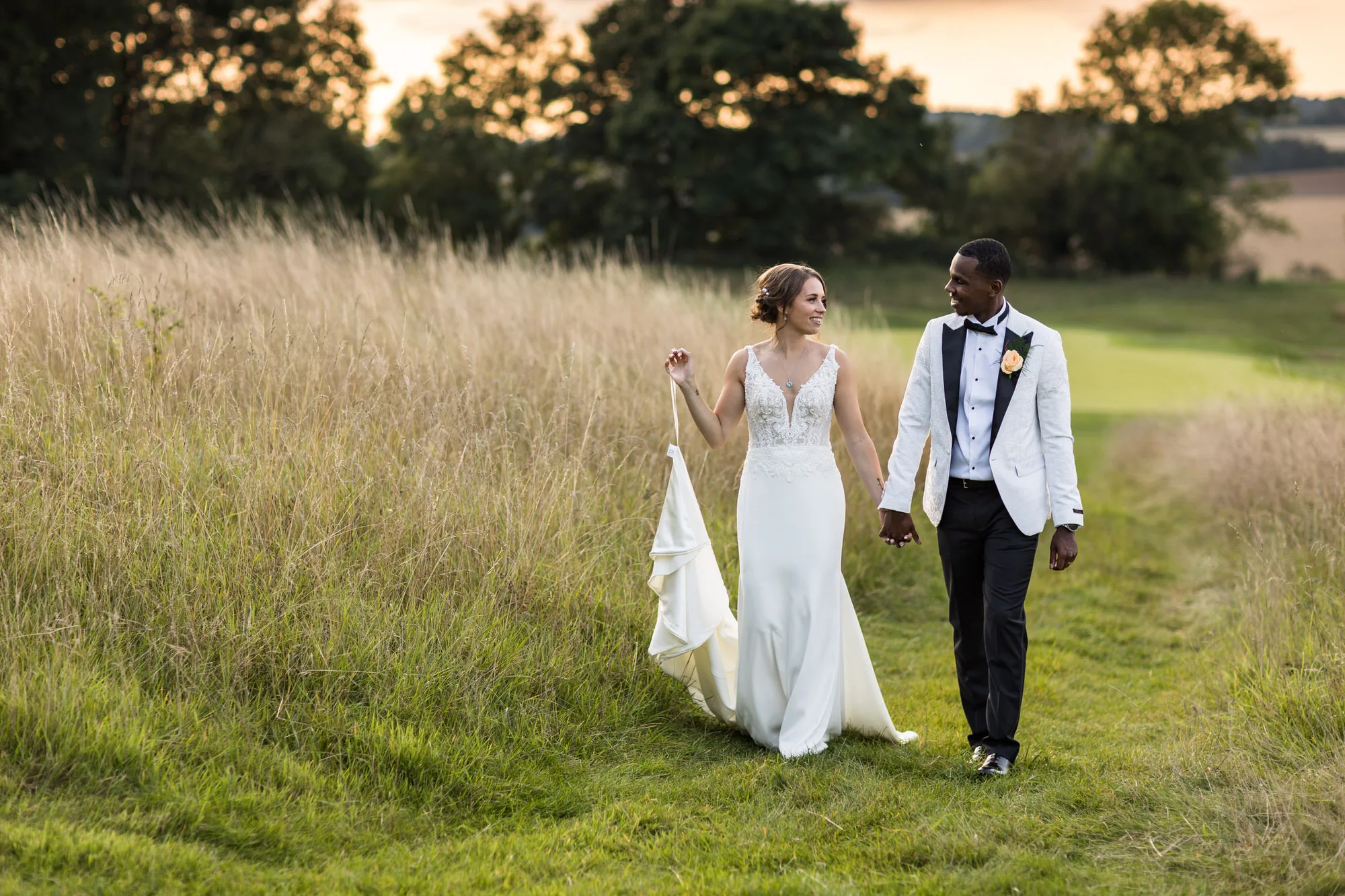documentary style wedding photography - bride and groom, walking in fields with sunset in the background.