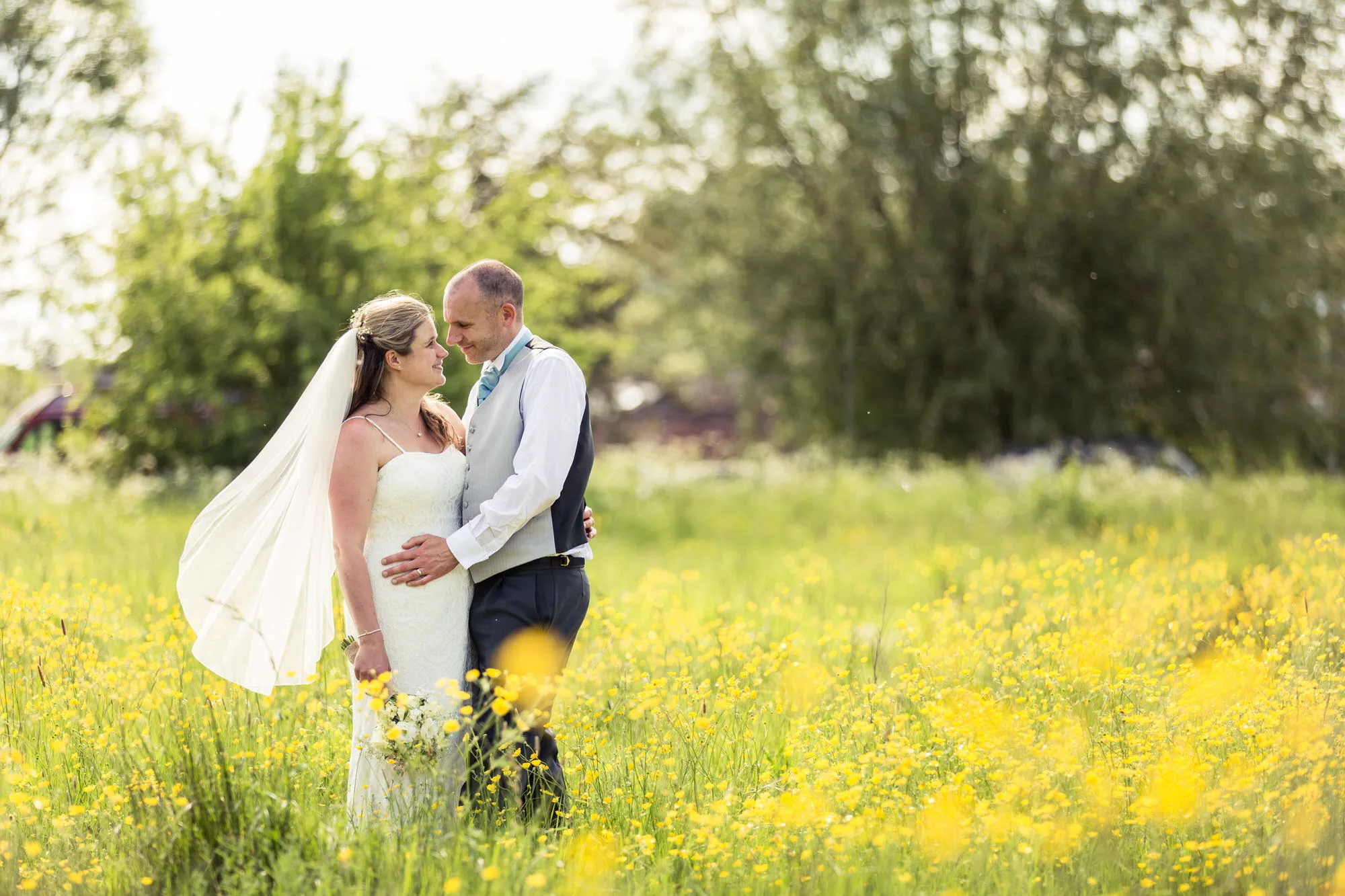 Questions to ask your wedding photographer - bride and groom stand in a meadow covered with yellow flowers.