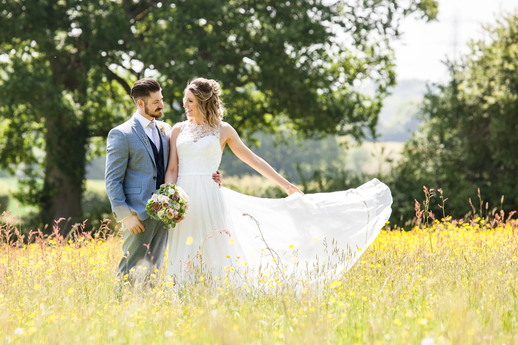 Reportage Wedding Photographer - a bride and groom stand together in a Summer meadow of yellow wildflowers 