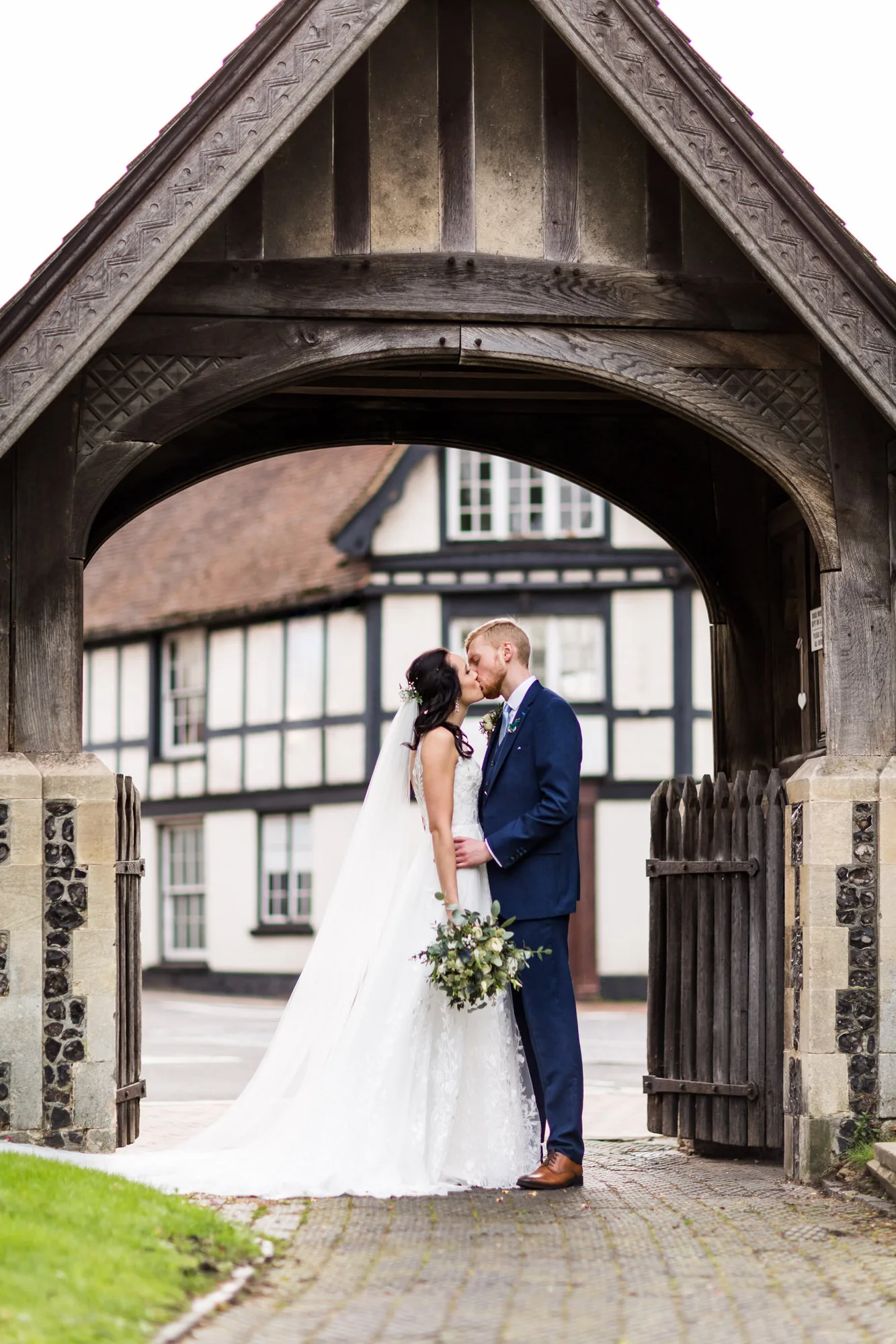 Surrey wedding photographer - bride and groom kiss under a Lychgate in bookham in Surrey