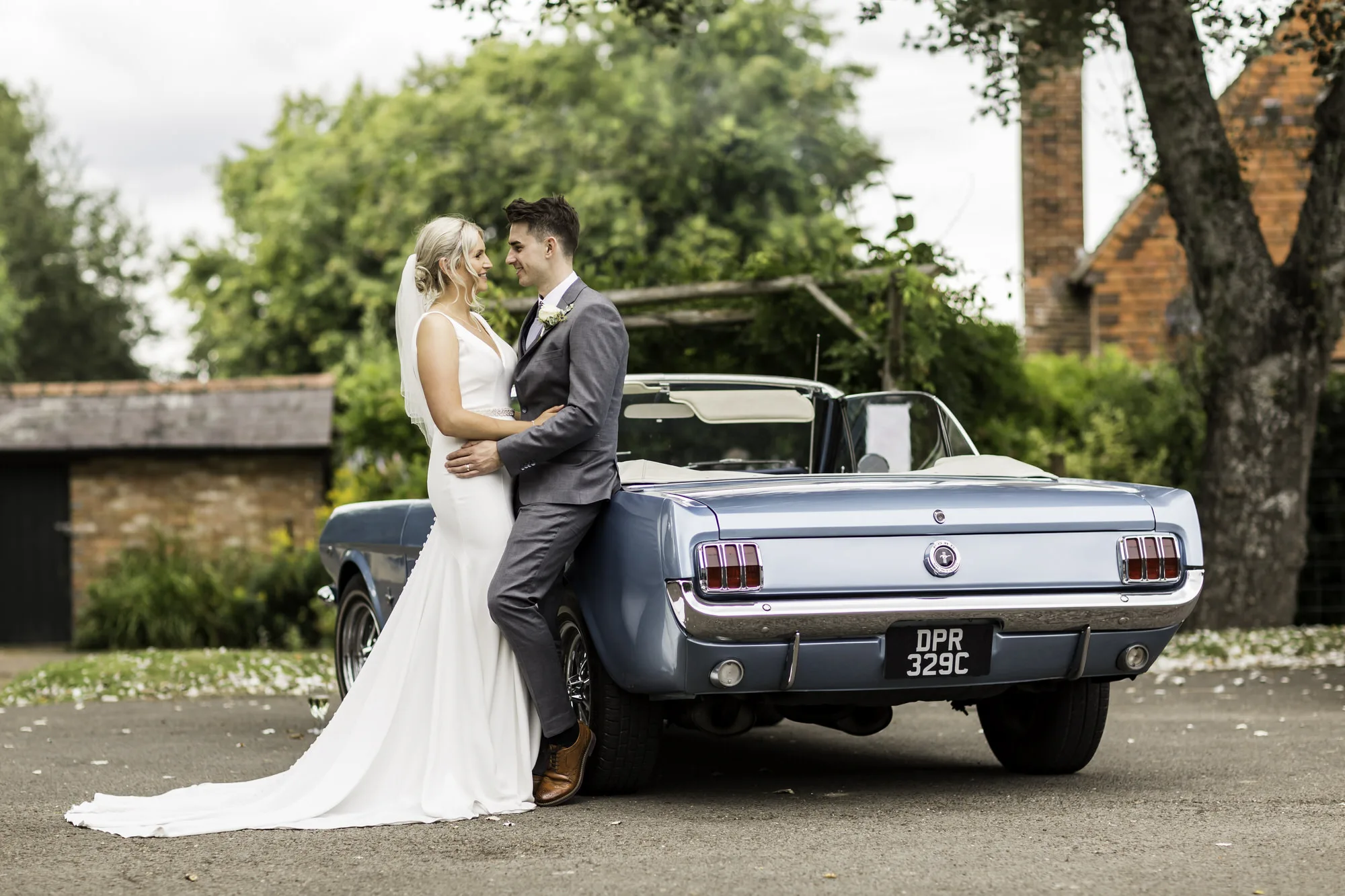 Sussex wedding photographer - bride and groom post together with blue Mustang wedding car at a pub in West Sussex