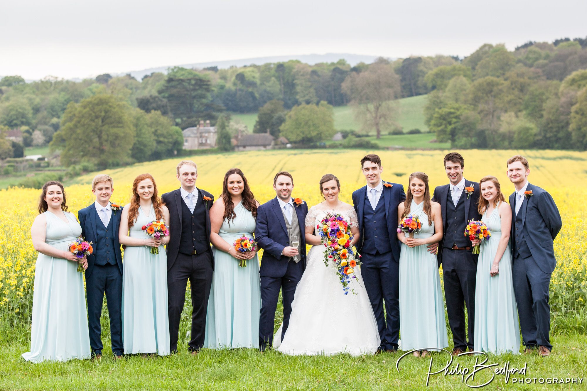Fitzleroi Barn wedding photographer - bridal party group photograph with West Sussex countryside in the background.