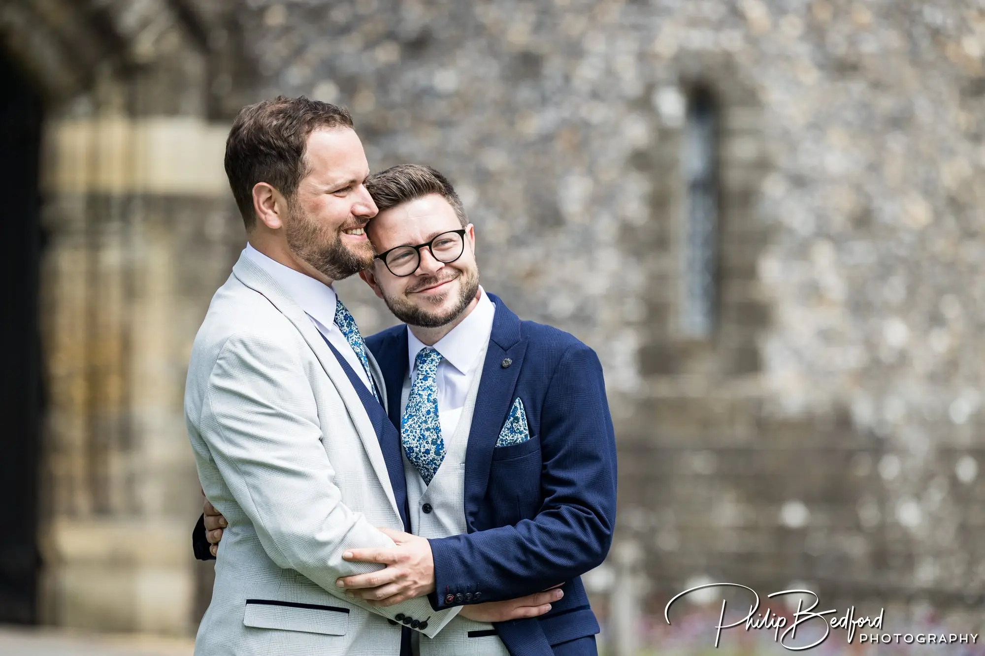 Two men on their wedding day embracing and looking happy with a backdrop of Arundel Castle