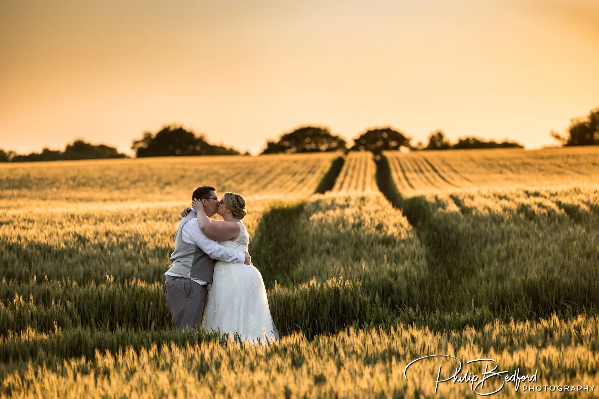 Bride and groom share a kiss in a Wheatfield at golden hour - Fitzleroi Barn Summer Wedding